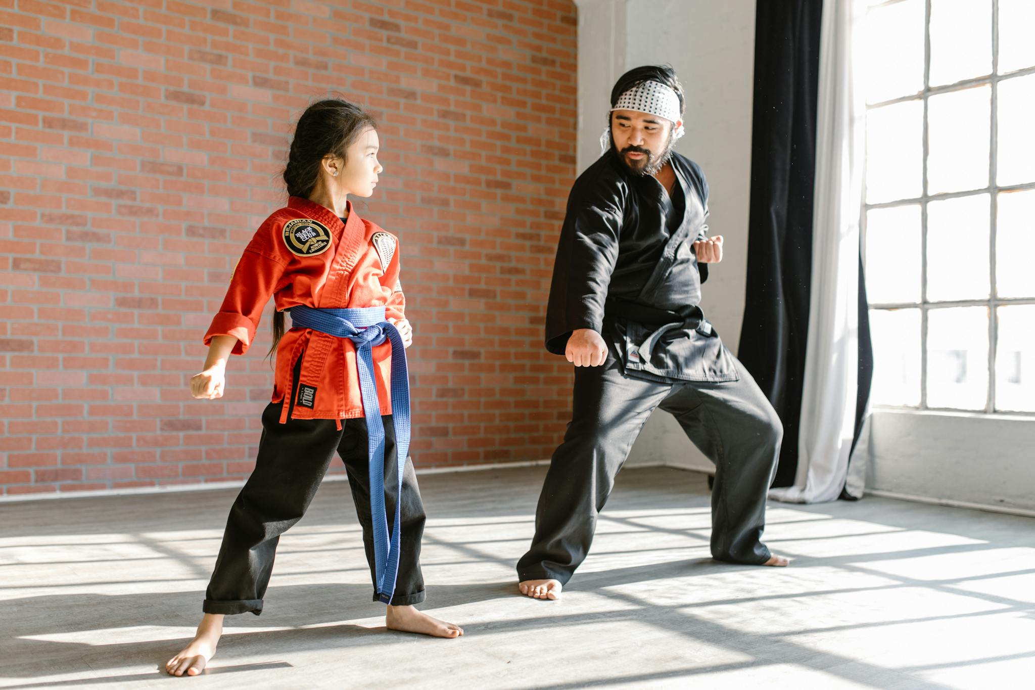 A child practicing martial arts with an adult instructor in a sunlit dojo.
