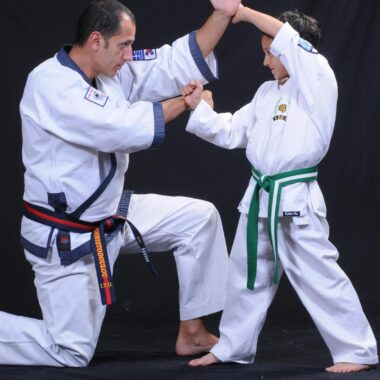 An instructor and child practicing martial arts techniques in traditional uniforms.
