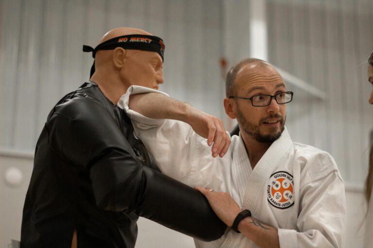 An instructor teaches self-defense using a martial arts dummy indoors.