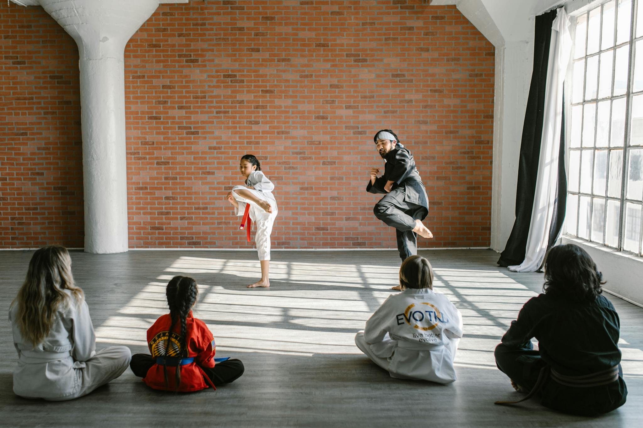 Children practicing martial arts with their instructor in a well-lit dojo.