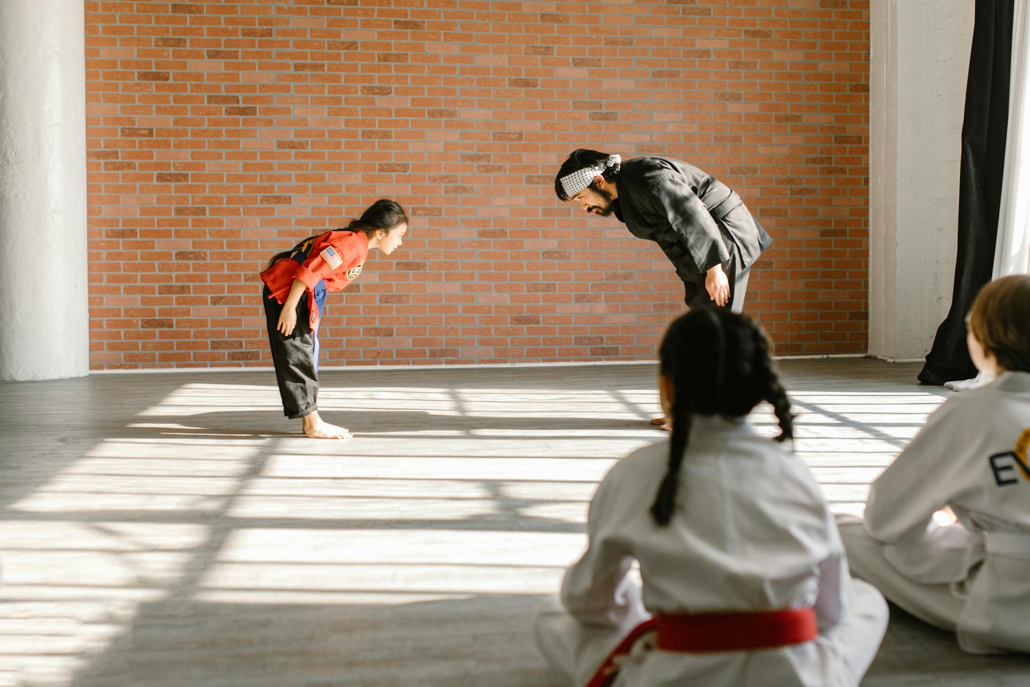 Instructor and children bowing during martial arts practice in dojo.
