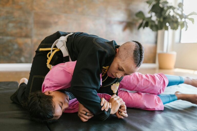 Instructor and student practicing martial arts techniques on a mat indoors.