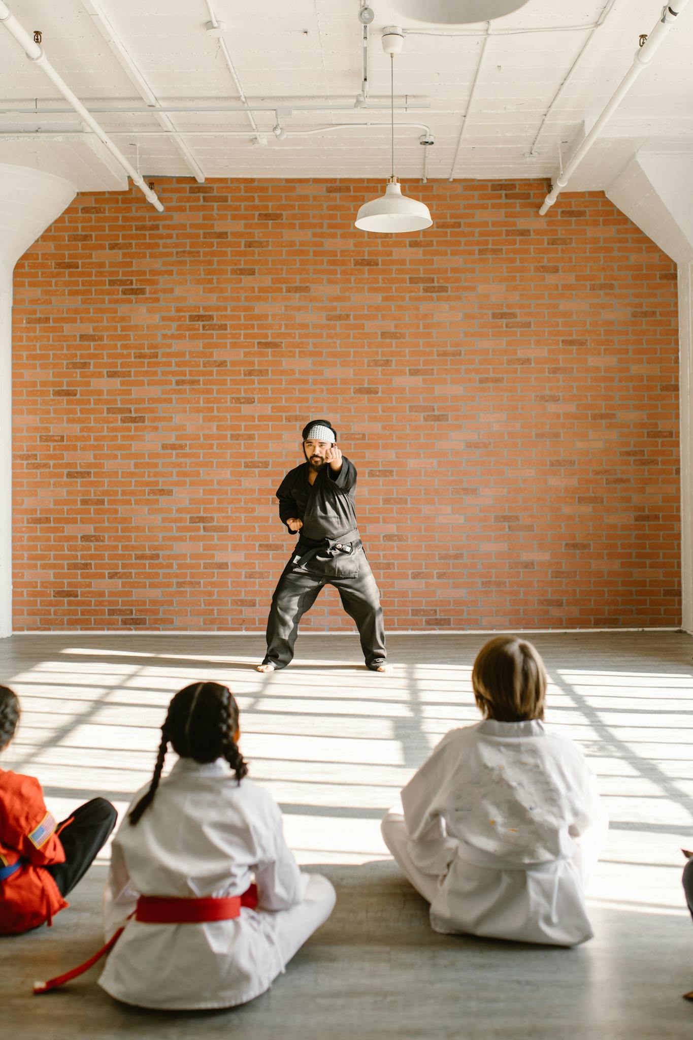 Karate instructor demonstrates techniques to attentive young students in a bright dojo.