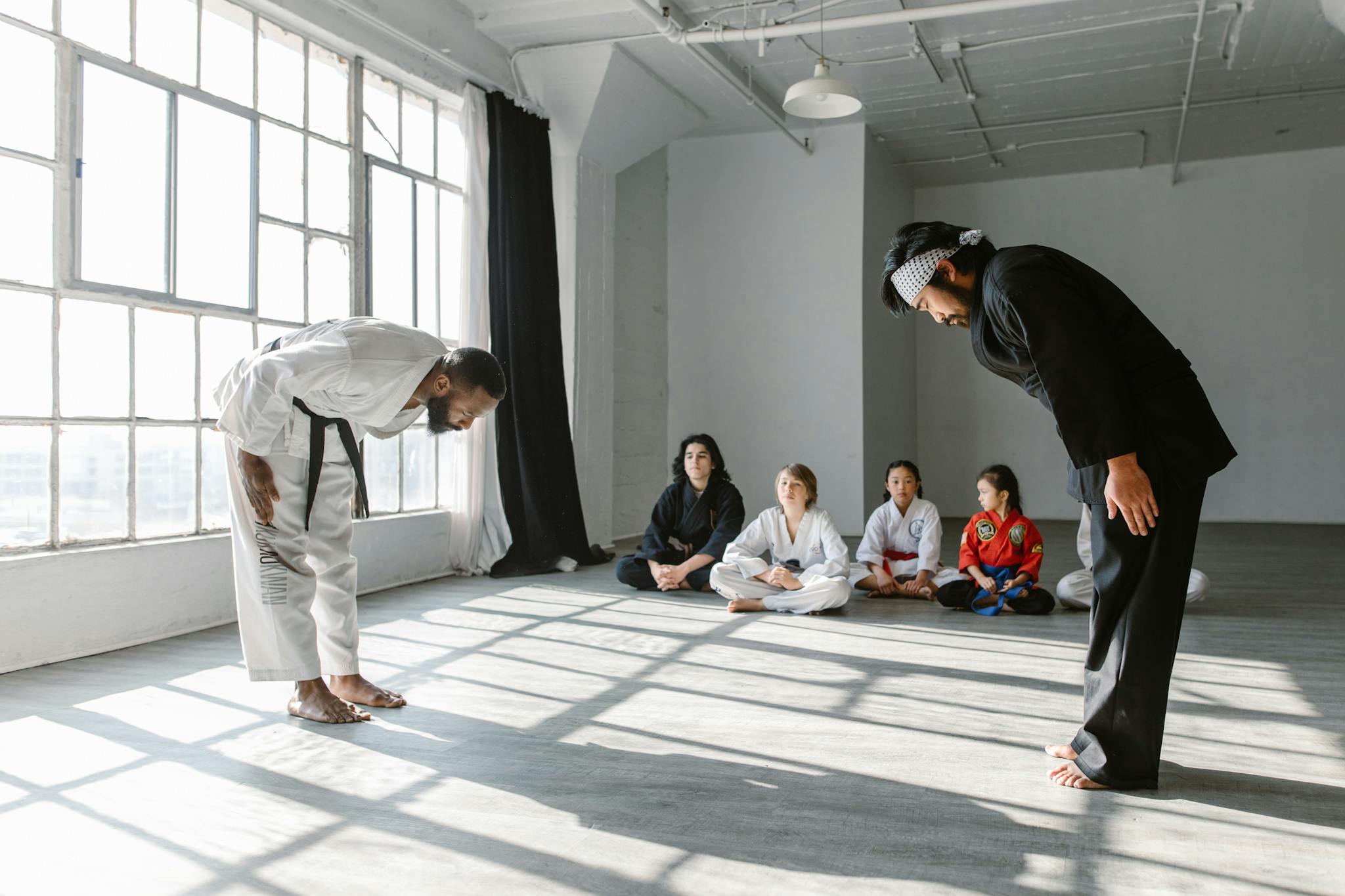 Martial arts practitioners in a dojo bowing as students watch, emphasizing discipline.